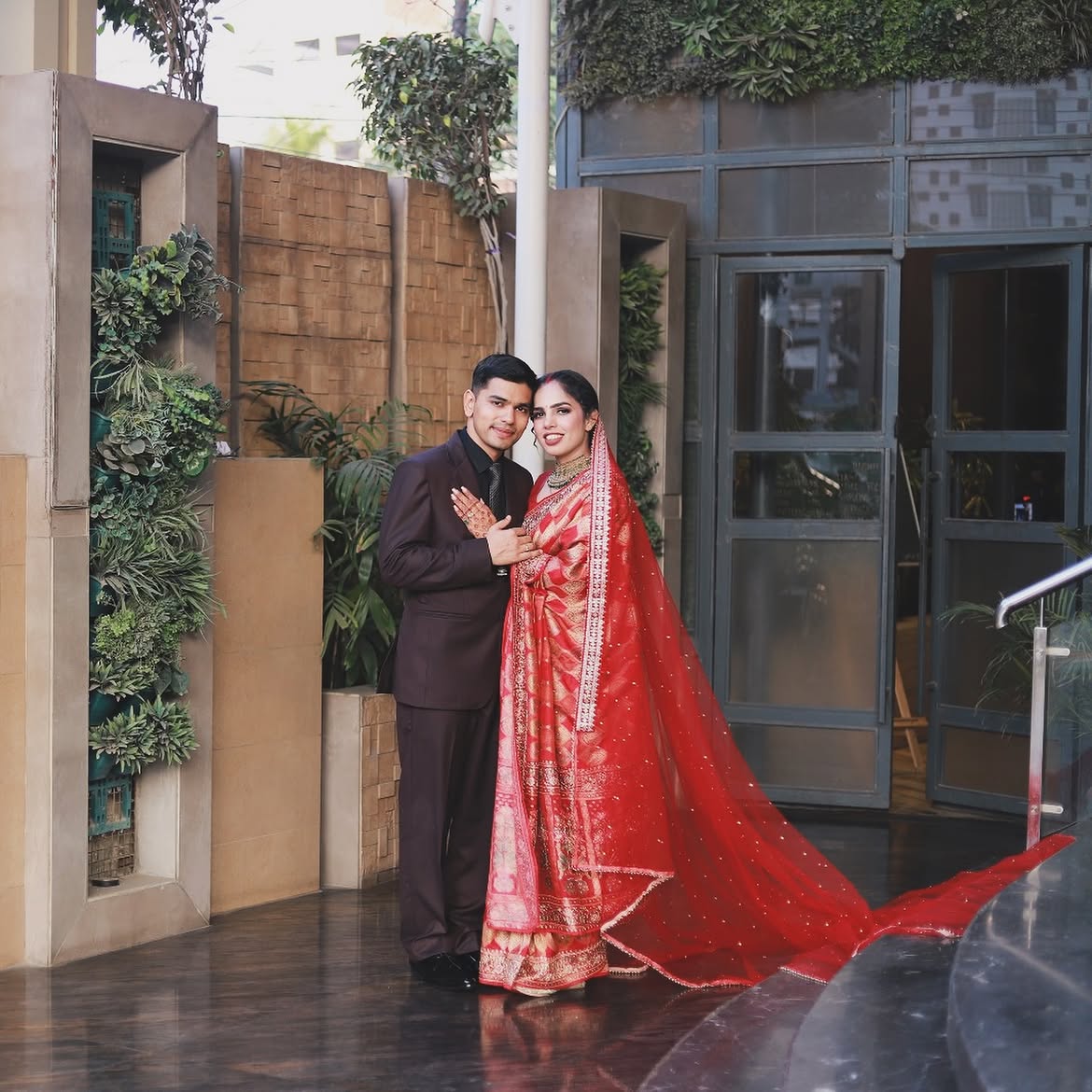 Newly married couple posing together, bride in a red banarasi saree with a long trail