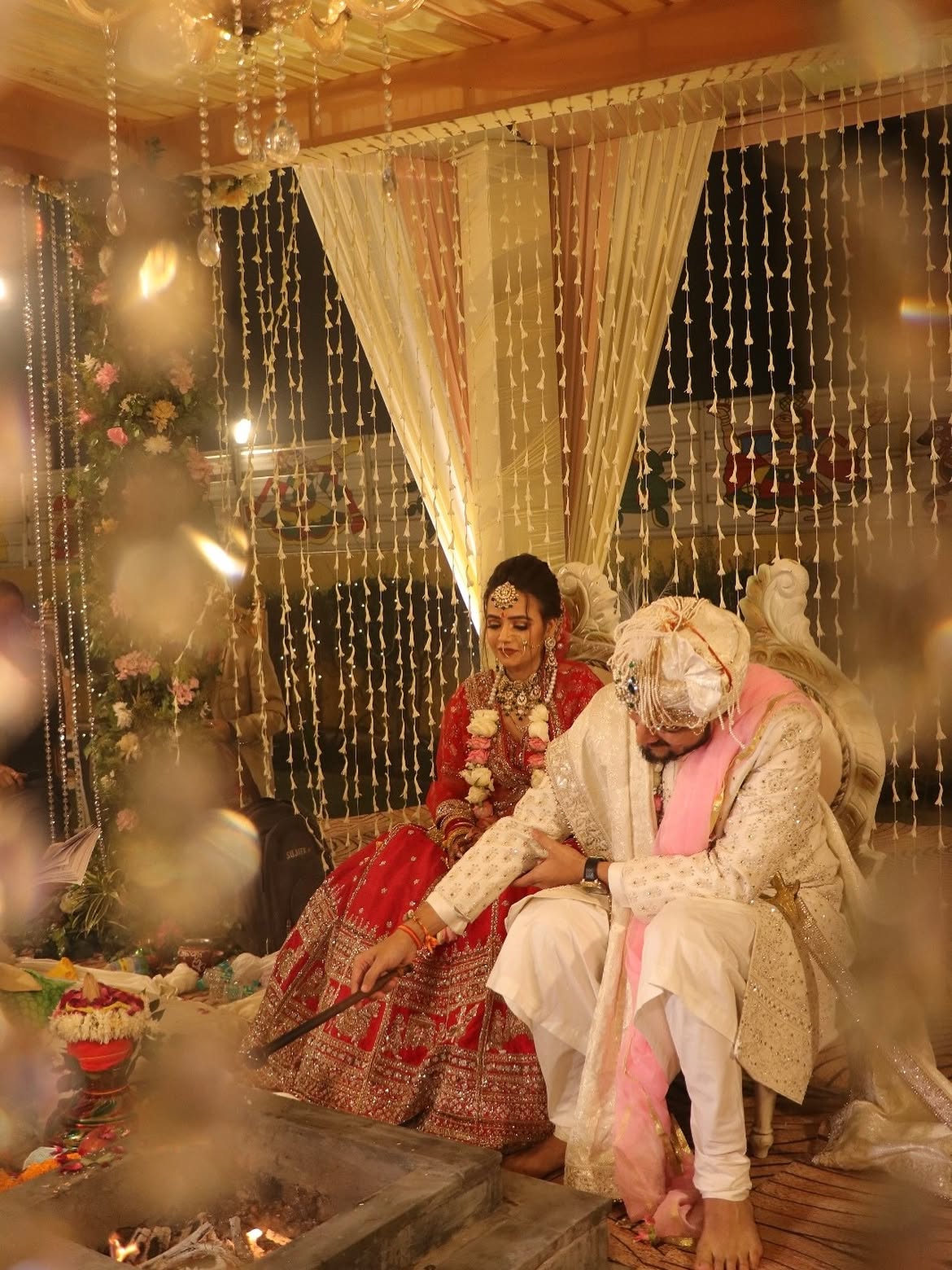 Bride and groom seated at the mandap during the wedding ceremony under floral drapes