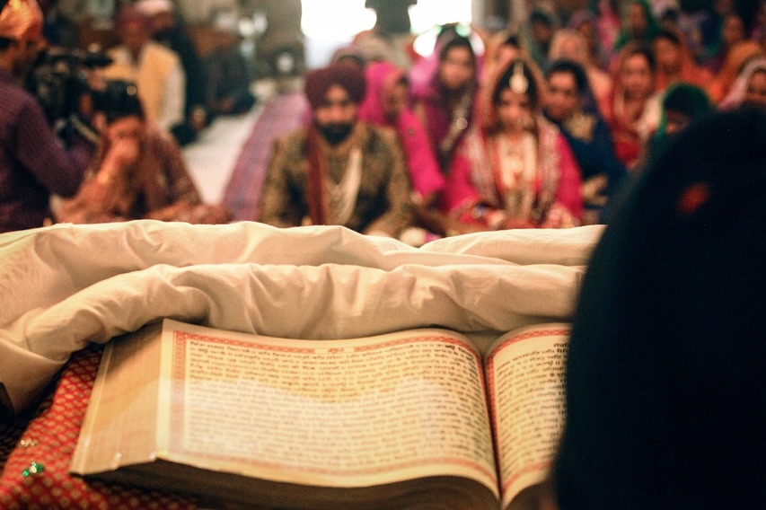 Sikh wedding ceremony with the Guru Granth Sahib in the foreground and the couple seated behind